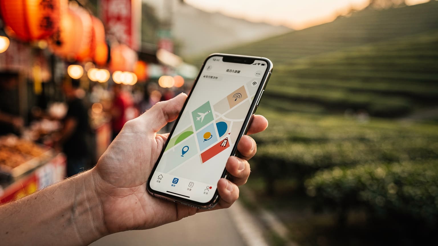 Close-up of a hand holding a smartphone displaying a data plan, with a blurred, warm-lit Taiwanese landscape in the background.